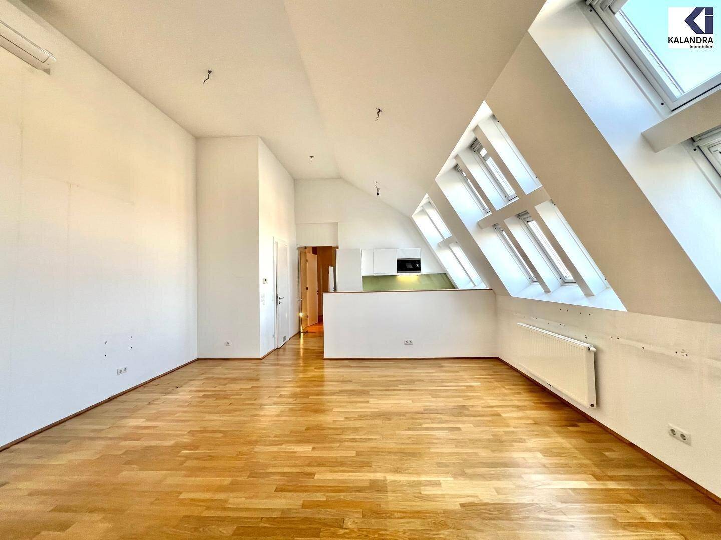 Geräumiger Wohnbereich mit Holzboden, Dachschrägen, Klimaanlage und Zugang zum Flur.
