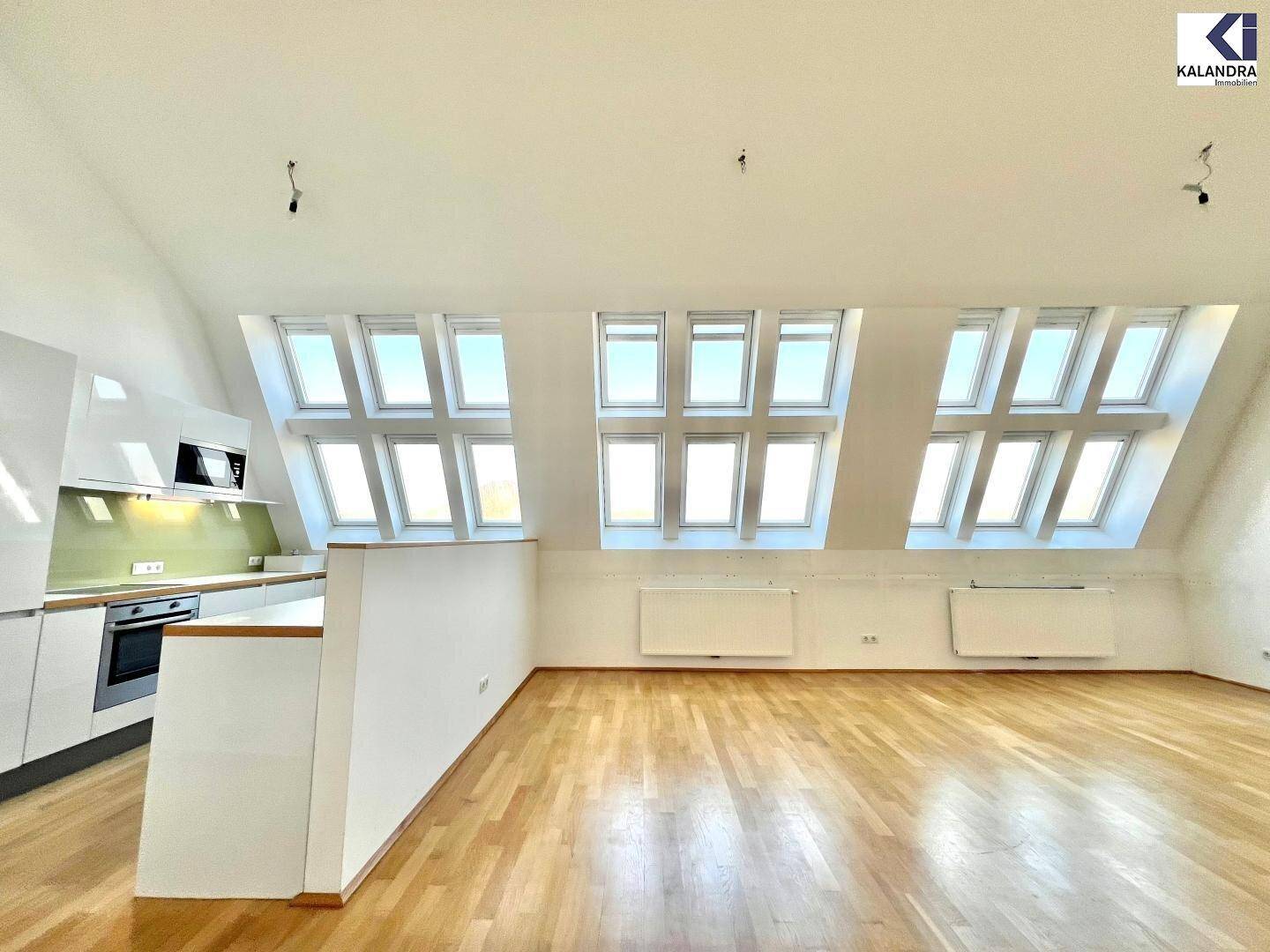 Offener Wohnbereich mit moderner Küchenzeile, Holzboden und vielen Dachfenstern für viel Licht.