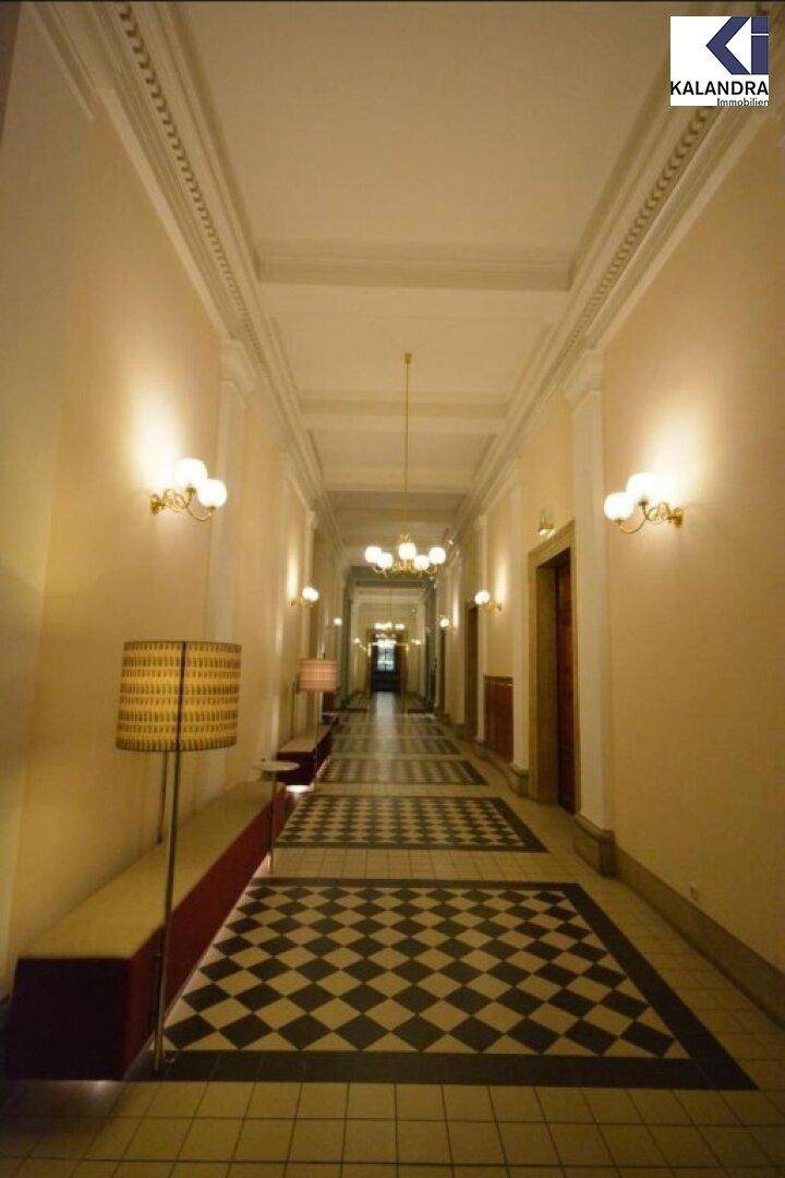 Langer, prunkvoller Flur mit gemustertem Fliesenboden, Wandlampen und einer Sitzbank in klassischem Stil.