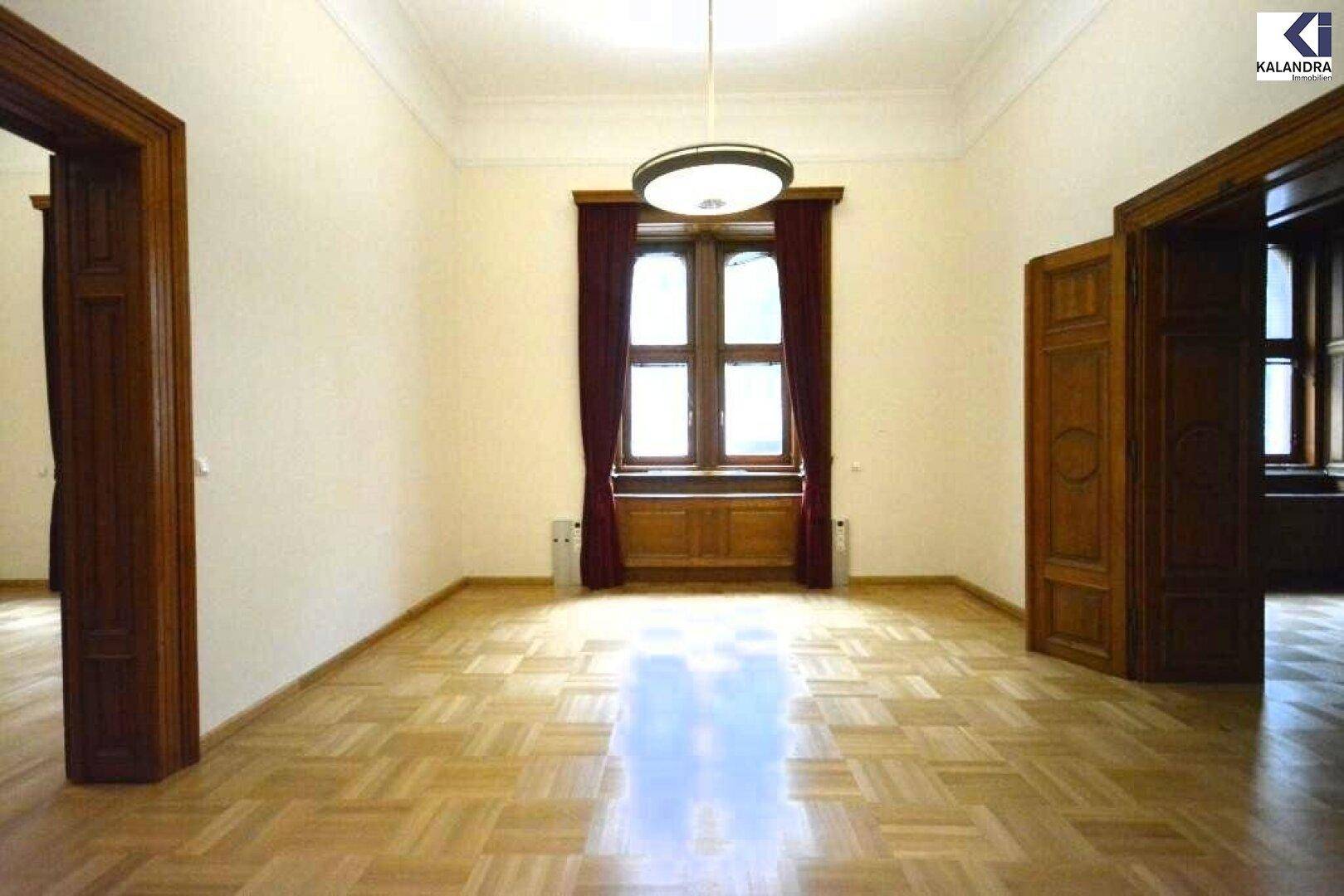 Heller Raum mit Parkettboden, hohen Decken und einem großen Fenster, das viel Tageslicht hereinlässt.