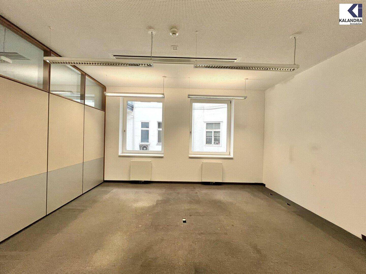 Leerer Büroraum mit zwei Fenstern und Teppichboden, bereit für die individuelle Gestaltung.