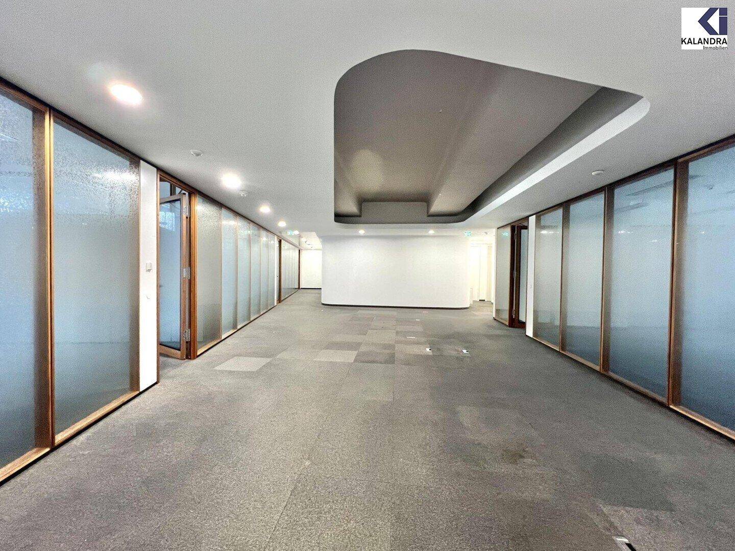 Langer Büroflur mit Glaswänden zu den einzelnen Büros und moderner Deckenbeleuchtung.