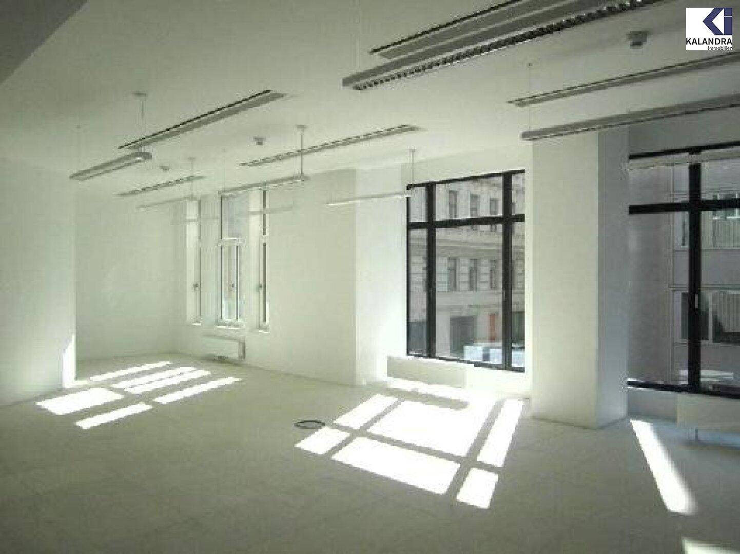 Heller Büroraum mit großen Fenstern, die viel Tageslicht hereinlassen und Schatten werfen.