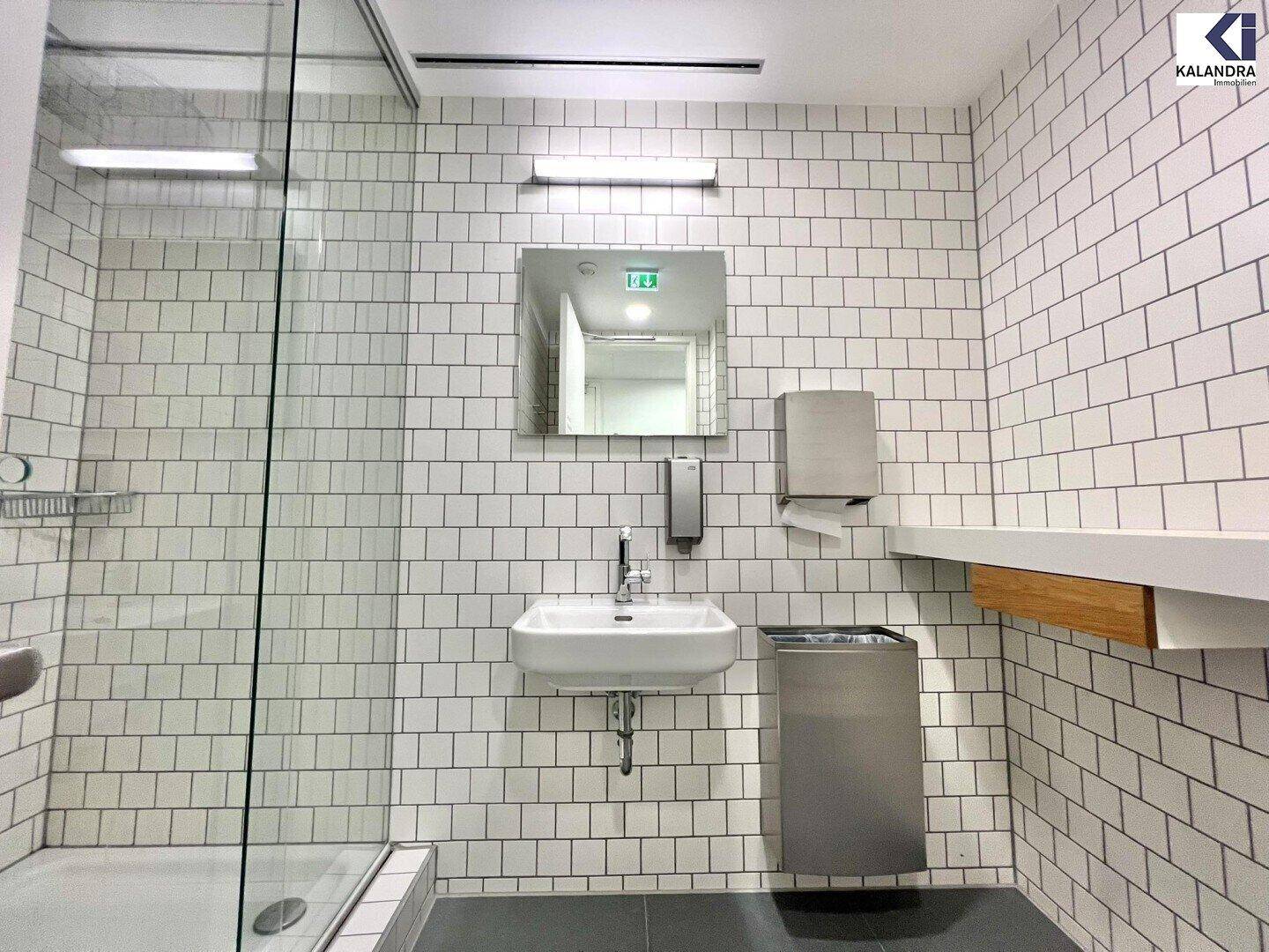 Modernes Badezimmer mit Duschkabine, Waschbecken und weißen Fliesen, gut beleuchtet.