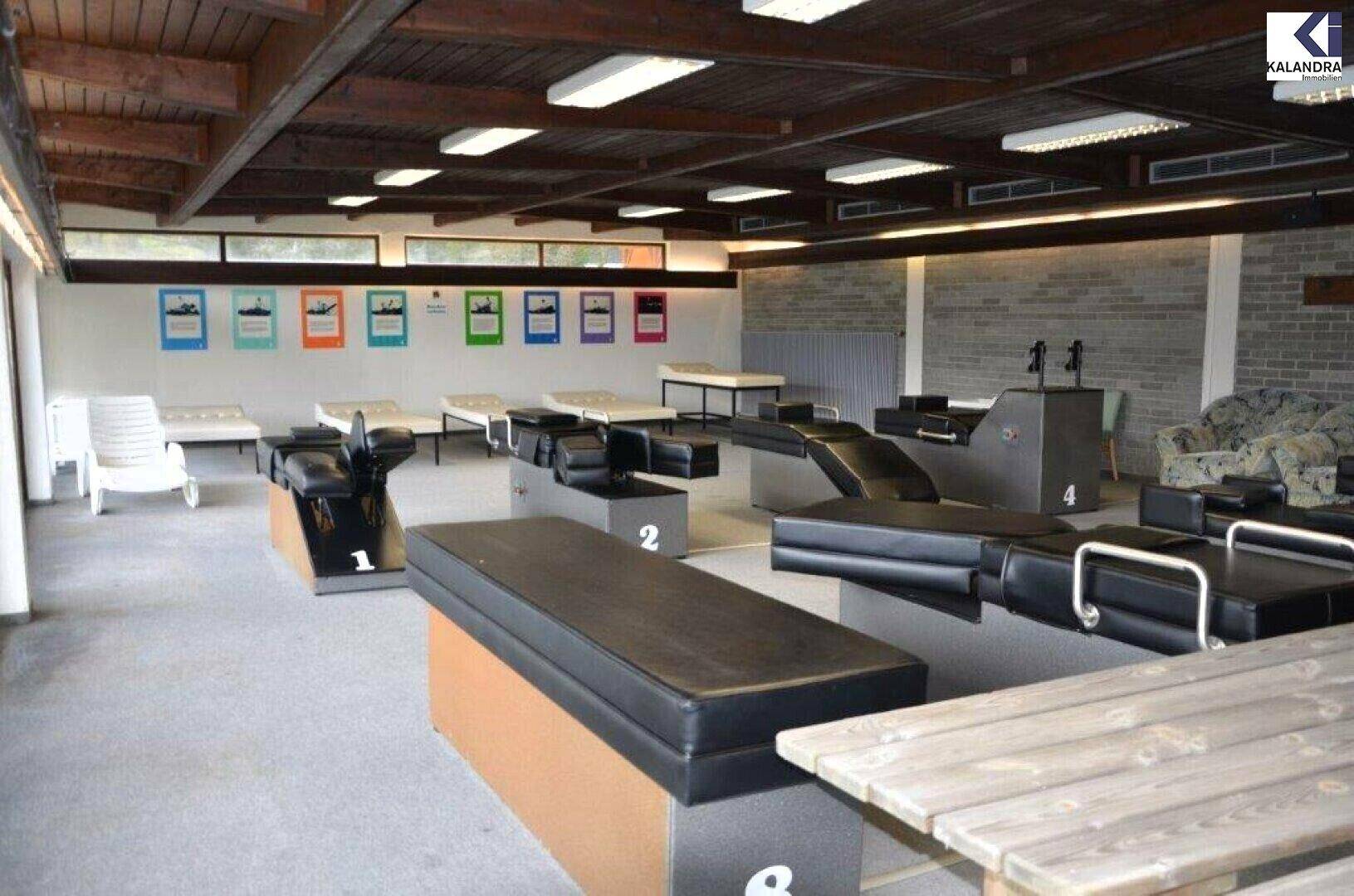 Großer Raum mit verschiedenen Trainings- oder Therapiegeräten, Betten und einem Holztisch, ideal für Aktivitäten.