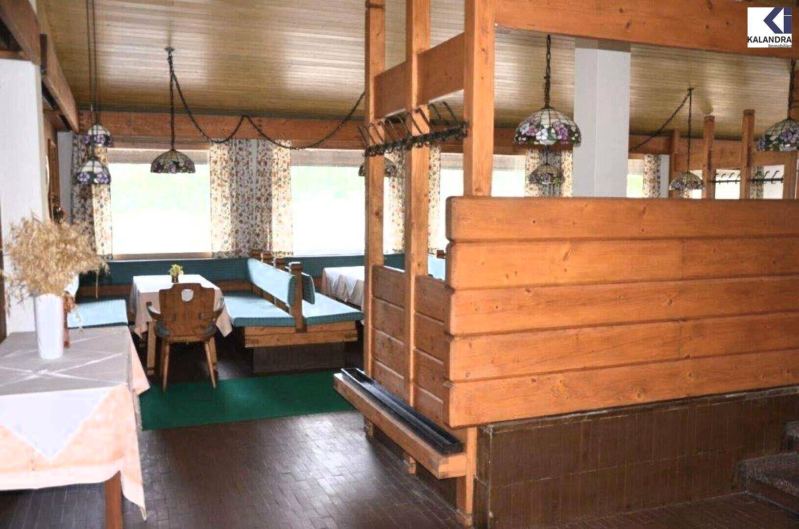 Rustikaler Innenbereich mit Holztäfelung, blauen Sitzbänken und Tischen, beleuchtet von dekorativen Hängelampen.