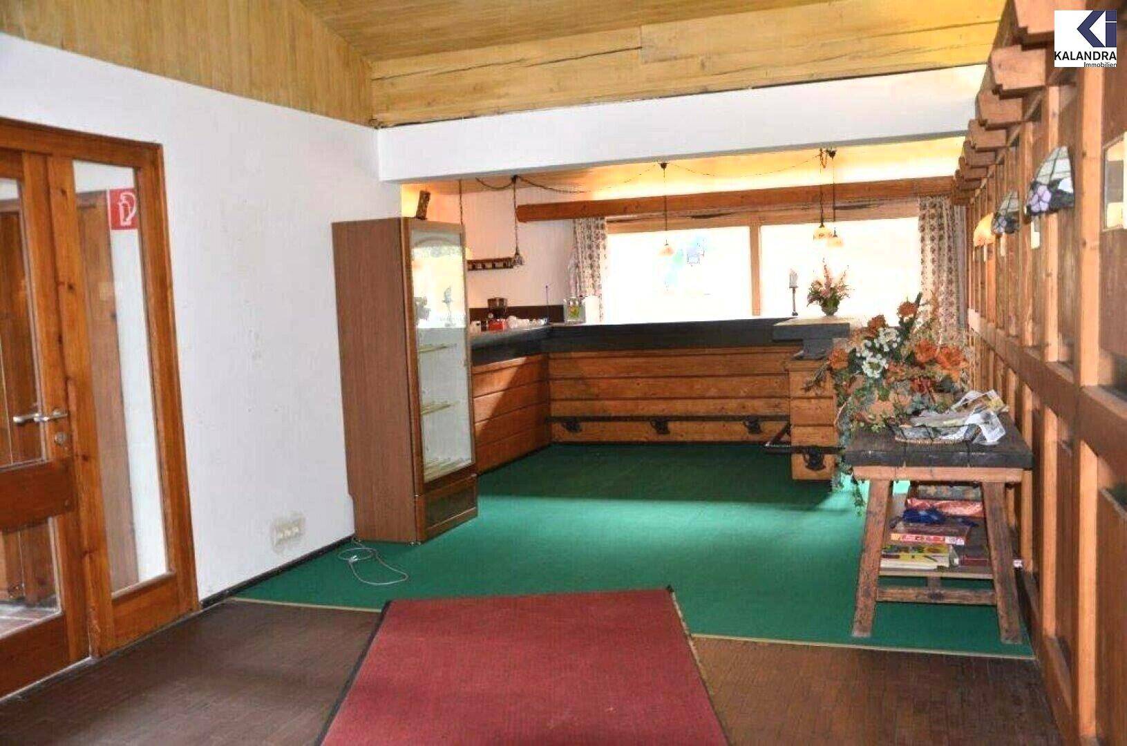 Innenbereich mit Holztheke, Vitrine und grünem Teppichboden, umgeben von Holztüren und -verkleidungen.