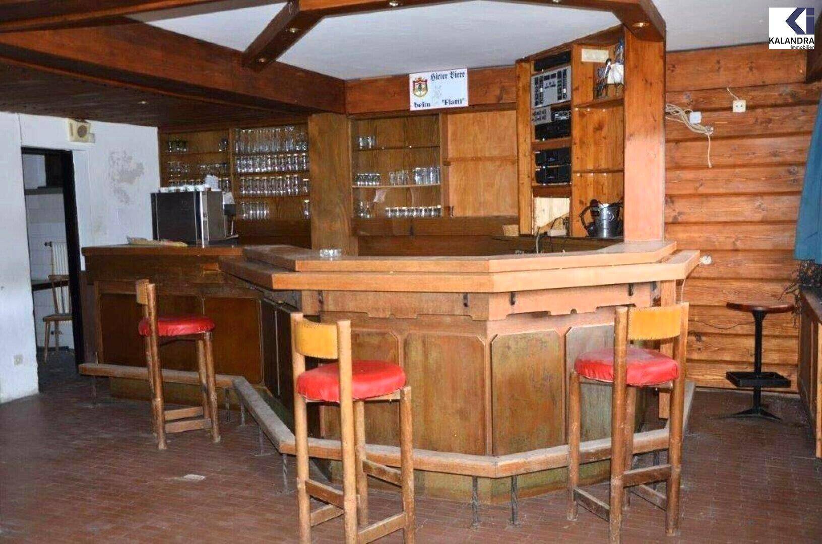 Rustikaler Barbereich aus Holz mit Barhockern, Regalen für Gläser und einer Kaffeemaschine.