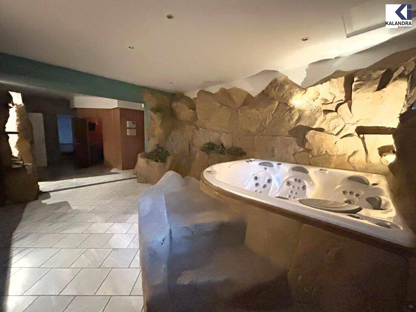 Innenbereich mit großem Whirlpool, umgeben von künstlichen Felsformationen und Fliesenboden.