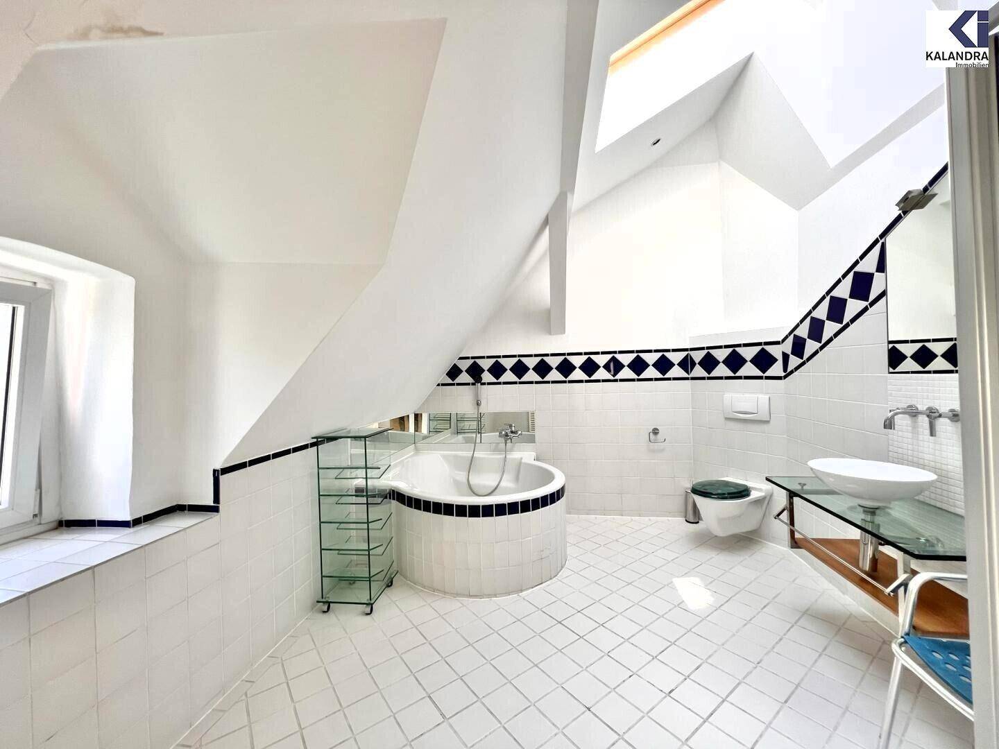 Großes Badezimmer im Dachgeschoss mit Eckbadewanne, Fliesen und Dachfenster.