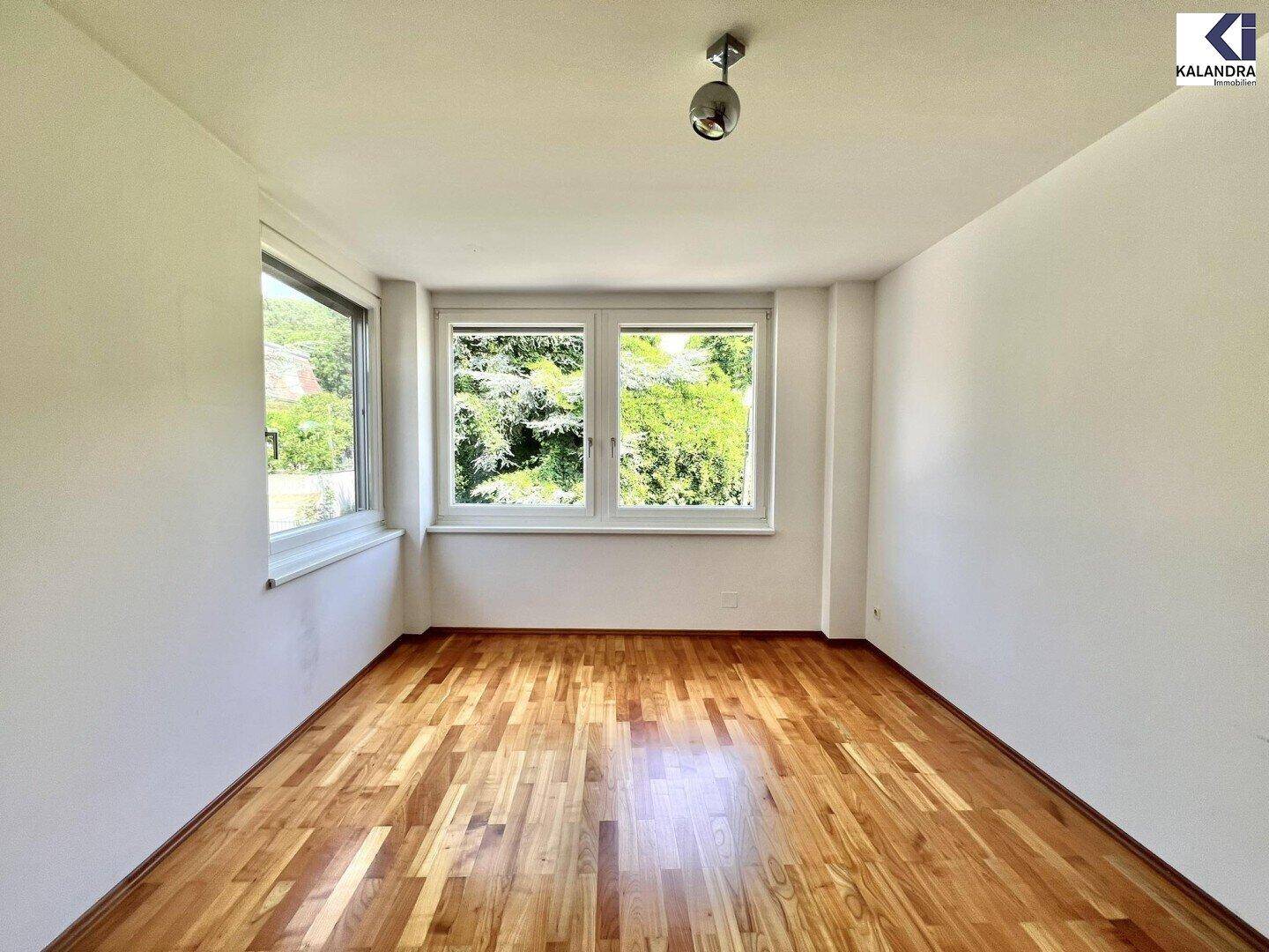Helles Schlafzimmer mit Holzboden und großen Fenstern, die viel Tageslicht hereinlassen.