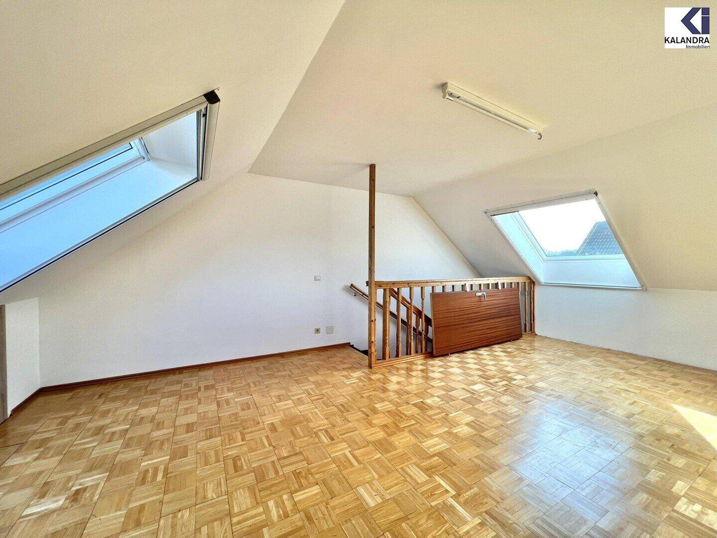 Helles Dachzimmer mit Parkettboden, Dachschrägen und zwei Dachfenstern.