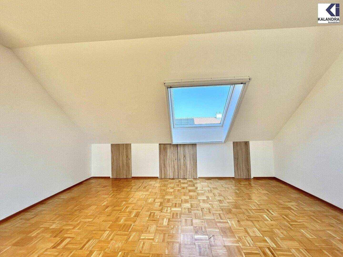 Großes Dachzimmer mit Parkettboden, Dachschrägen und einem zentralen Dachfenster.