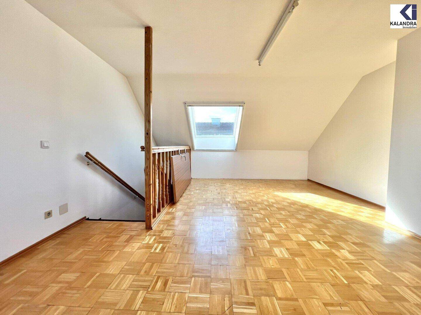 Geräumiges Dachzimmer mit Parkettboden, Dachschrägen und einem großen Dachfenster.