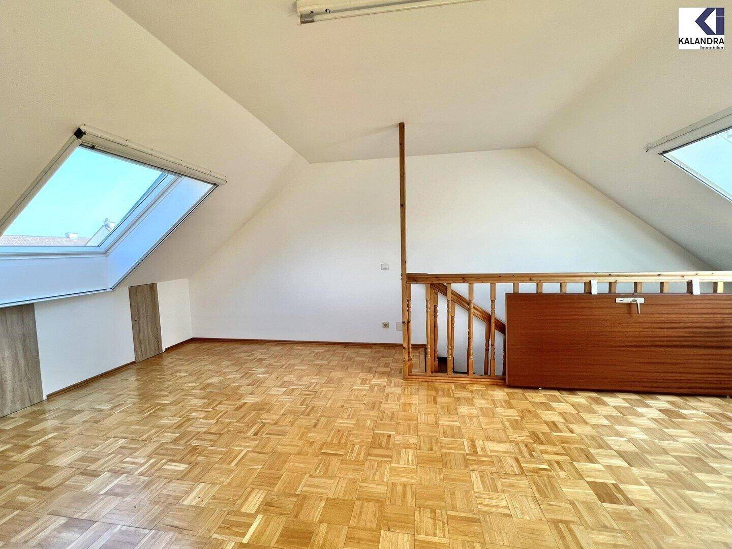 Helles Dachzimmer mit Parkettboden, Dachschrägen und zwei Dachfenstern.