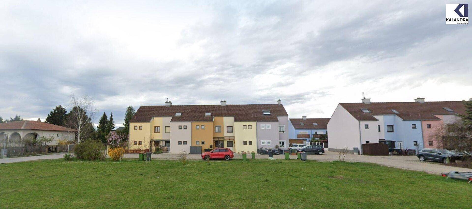 Weitläufige Ansicht einer Wohnsiedlung mit farbigen Reihenhäusern unter bewölktem Himmel.