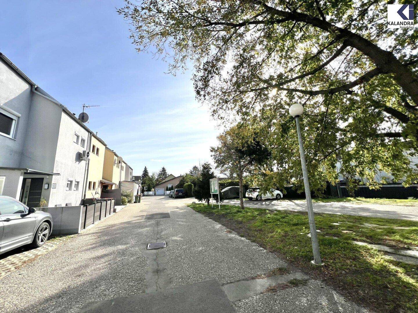 Ruhige Wohnstraße mit Reihenhäusern und geparkten Fahrzeugen unter blauem Himmel.