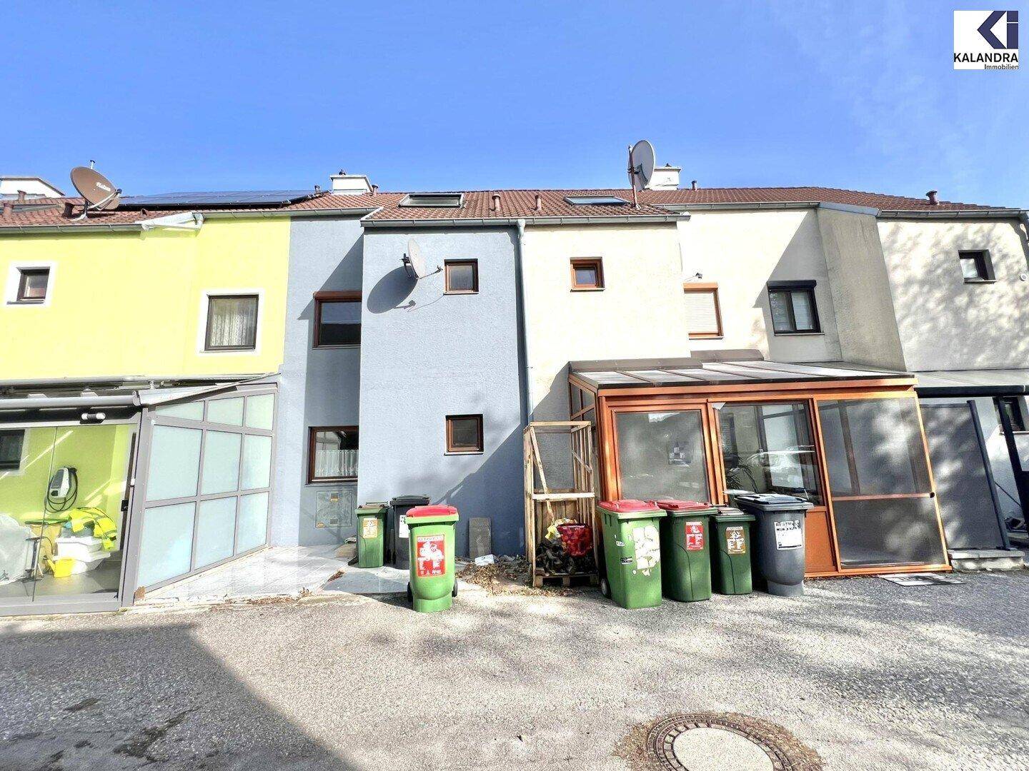 Rückseite der Reihenhäuser mit Anbauten und Mülltonnen im Außenbereich.