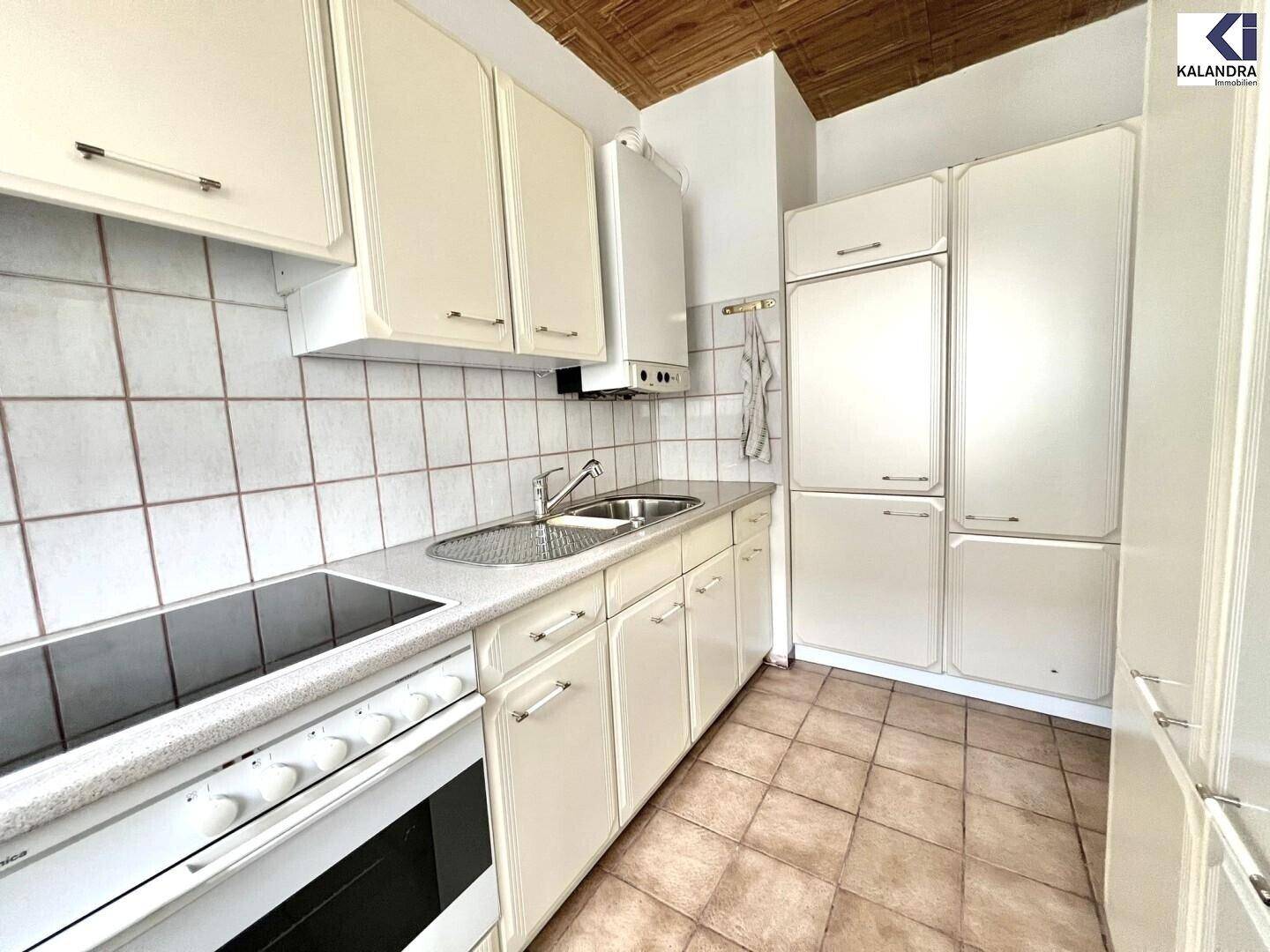 Funktionale Küche mit cremefarbenen Schränken, Spüle und einem Elektroherd.
