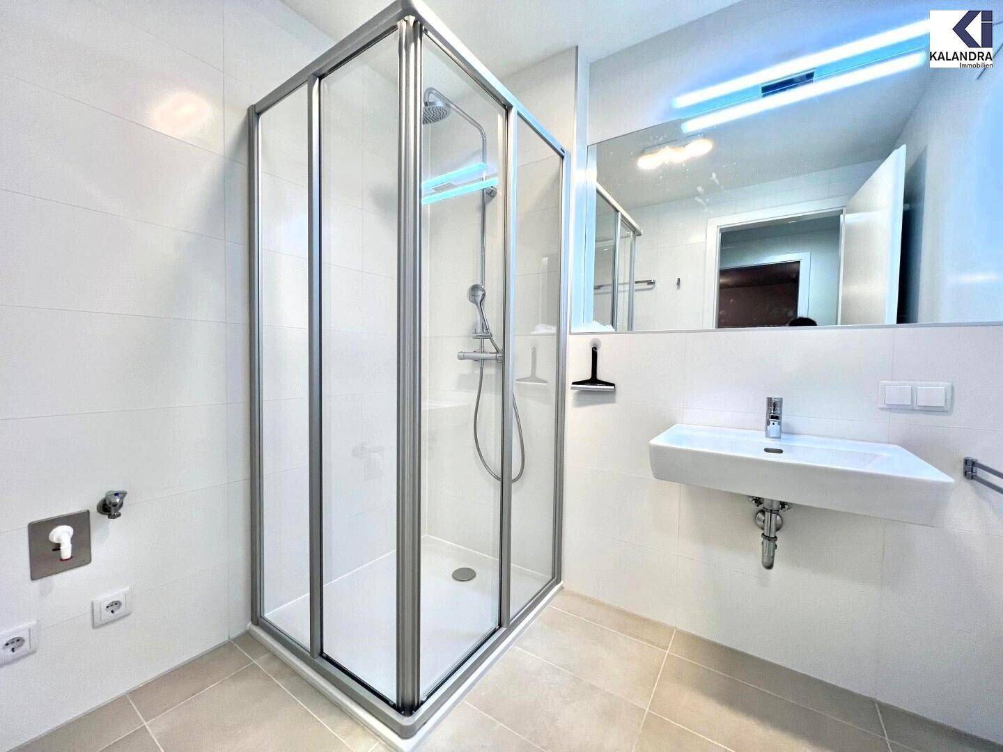 Modernes Badezimmer mit Duschkabine, Wandwaschbecken und hellen Fliesen.