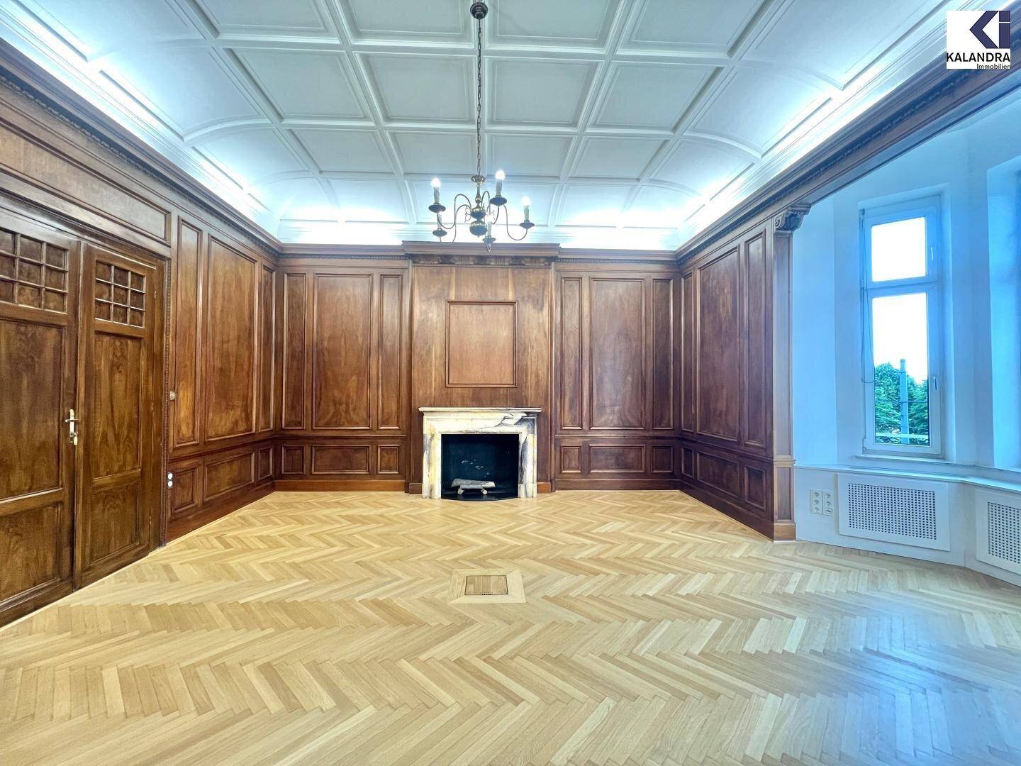 Repräsentativer Wohnraum mit Holztäfelung, Kamin und Kassettendecke, ausgestattet mit Fischgrätparkett.