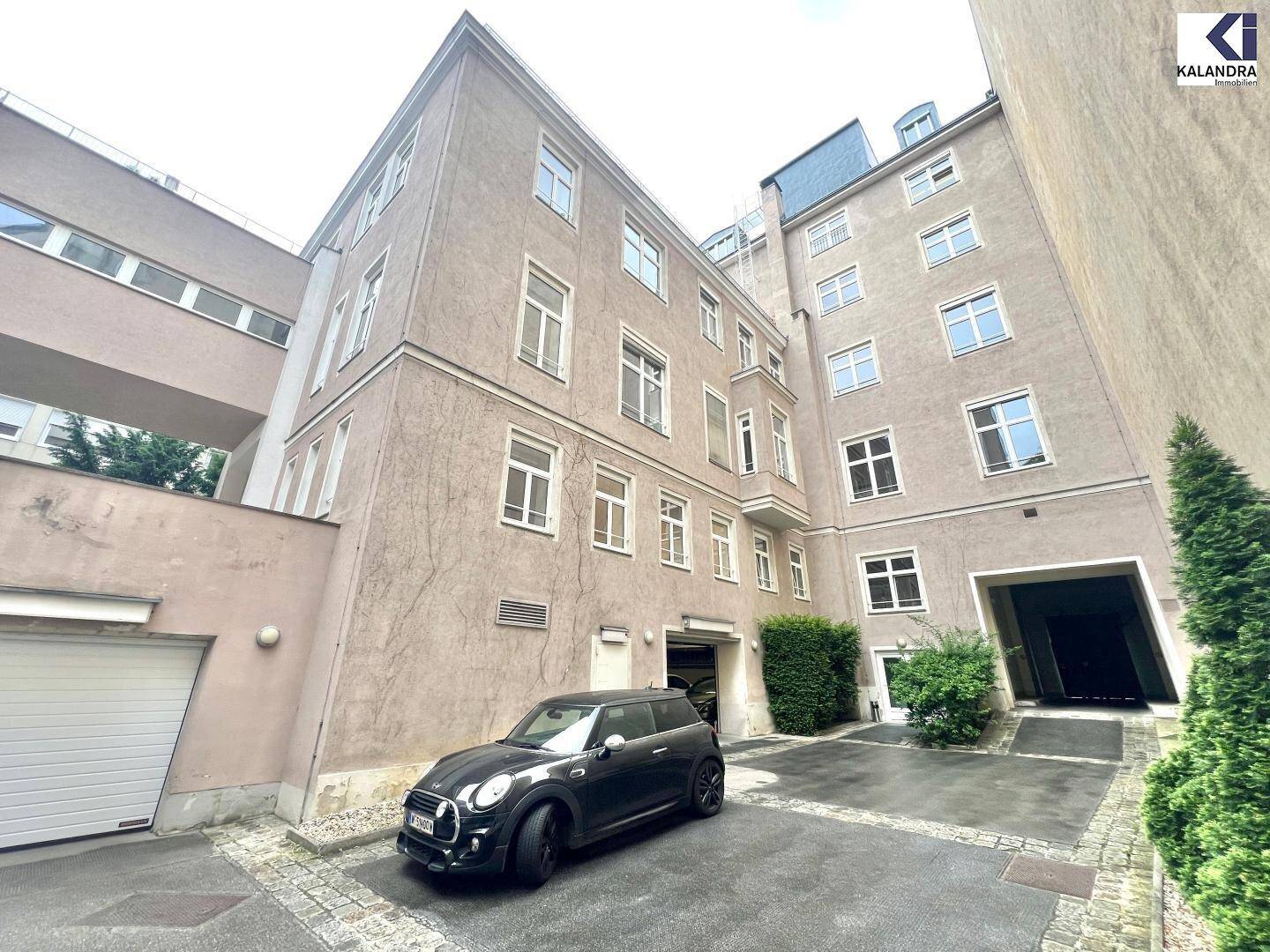 Hinterhofansicht eines Gebäudes mit Garagenzufahrt und geparktem Auto.