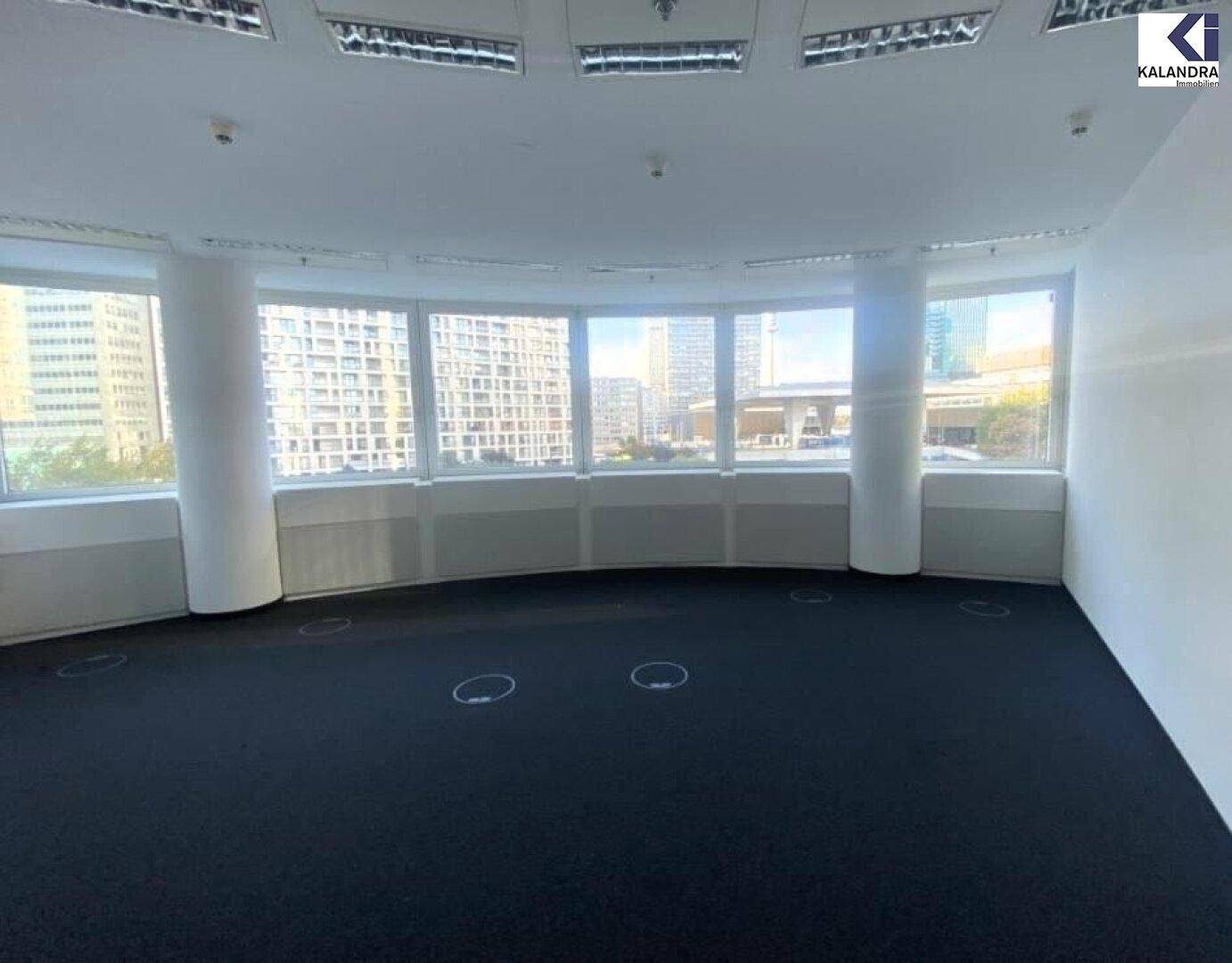 Geräumiges Büro mit gebogener Fensterfront, Teppichboden und Blick auf die Stadtlandschaft.