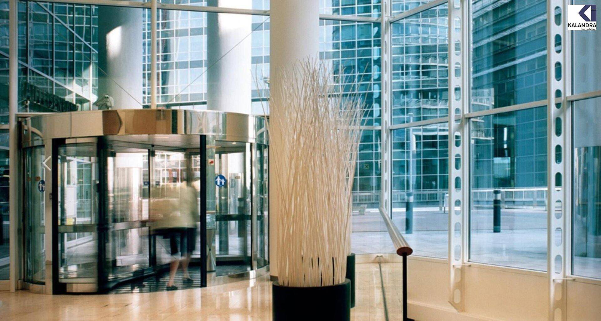 Moderner Eingangsbereich mit Drehtür, Glasfassade und dekorativer Säule in einem Bürogebäude.