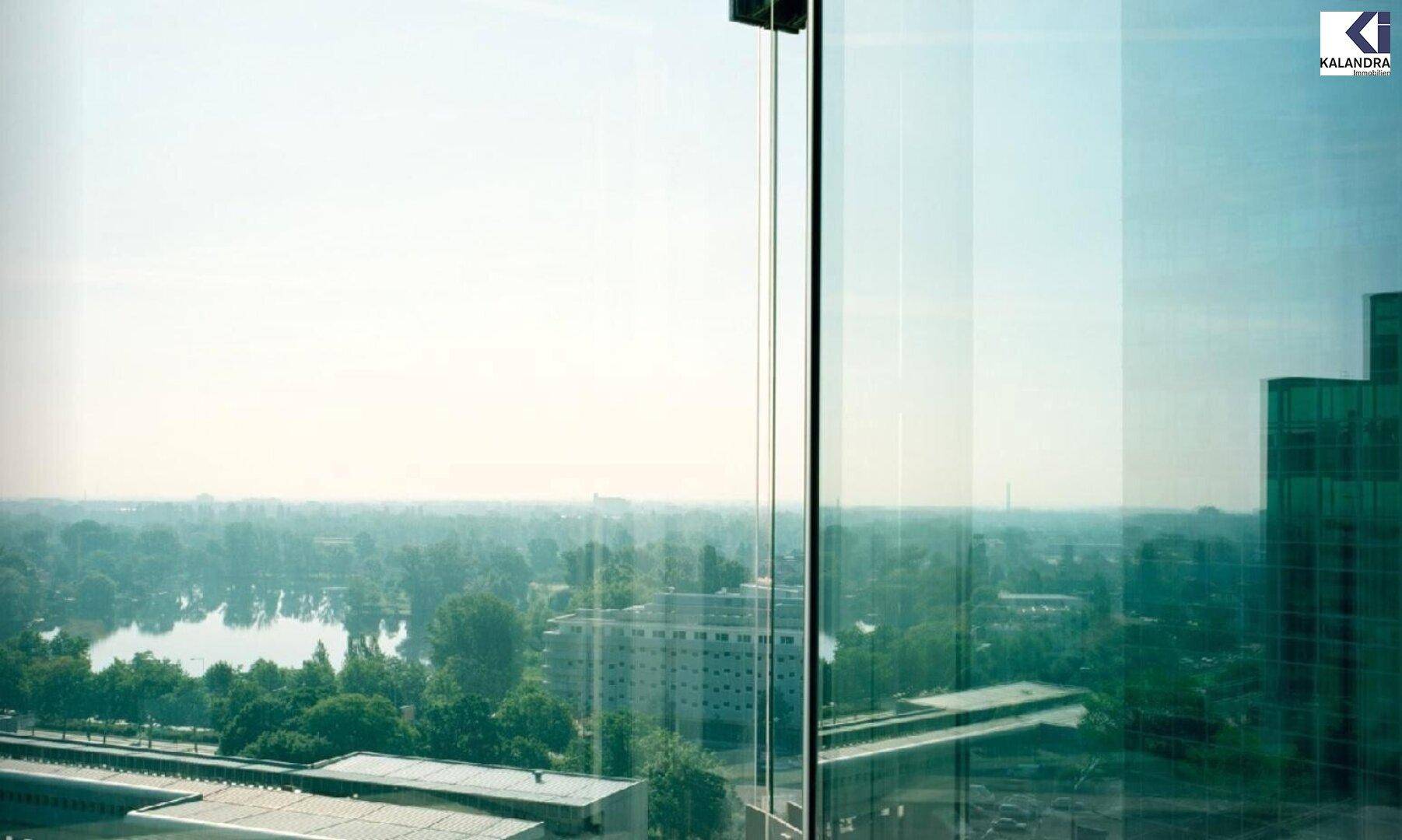 Weitblick aus einem Fenster über eine Stadtlandschaft mit See und viel Grün.