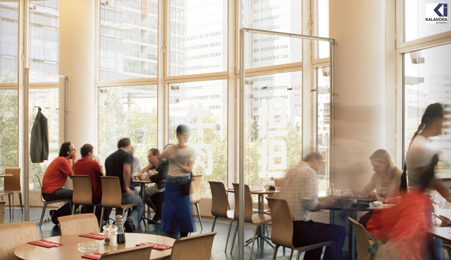 Helles Restaurant mit vielen Gästen, hohen Fenstern und moderner Einrichtung.