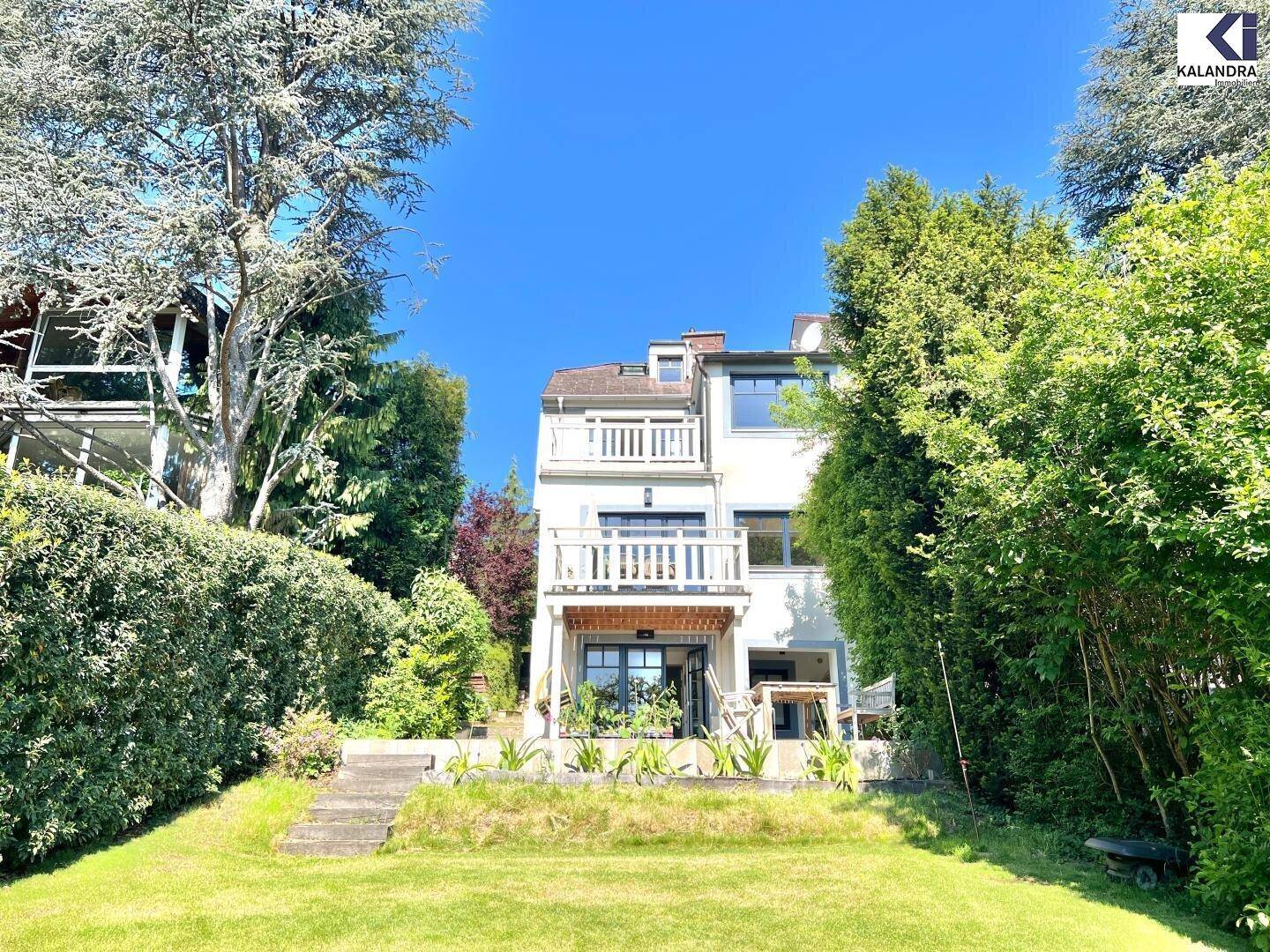 Fassade des Hauses vom Garten aus gesehen, mit mehreren Balkonen und einer kleinen Terrasse.