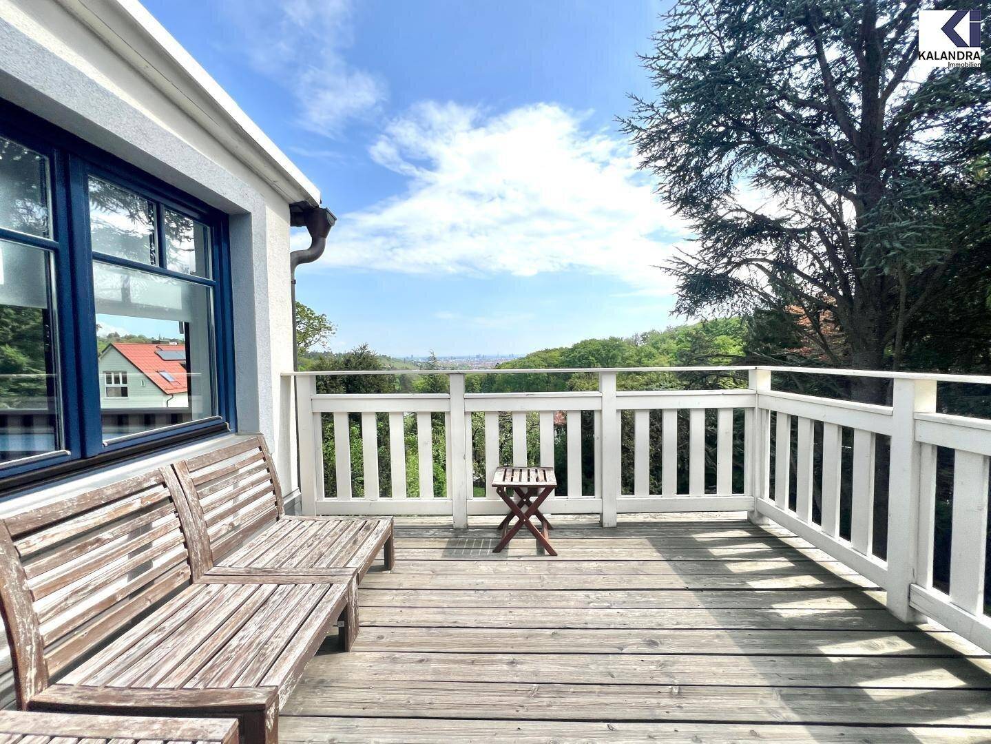 Geräumiger Holzbalkon mit Sitzbänken und weitem Blick über die grüne Landschaft.
