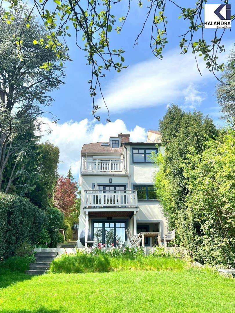 Rückansicht des Hauses mit mehreren Balkonen, umgeben von üppigem Grün und Bäumen.