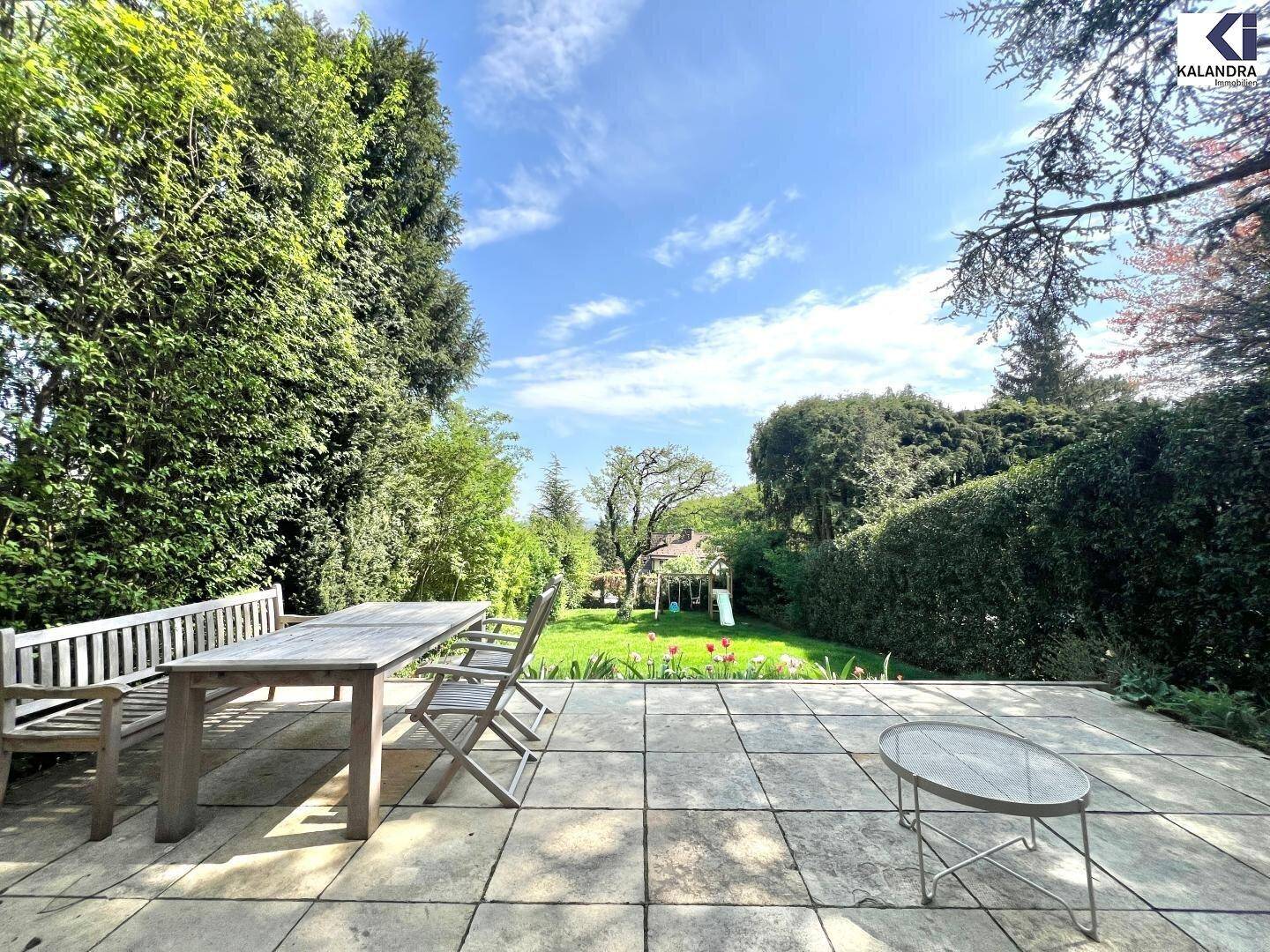 Große gepflasterte Terrasse mit Holztisch und Bänken, mit Blick auf den Garten und Spielplatz.