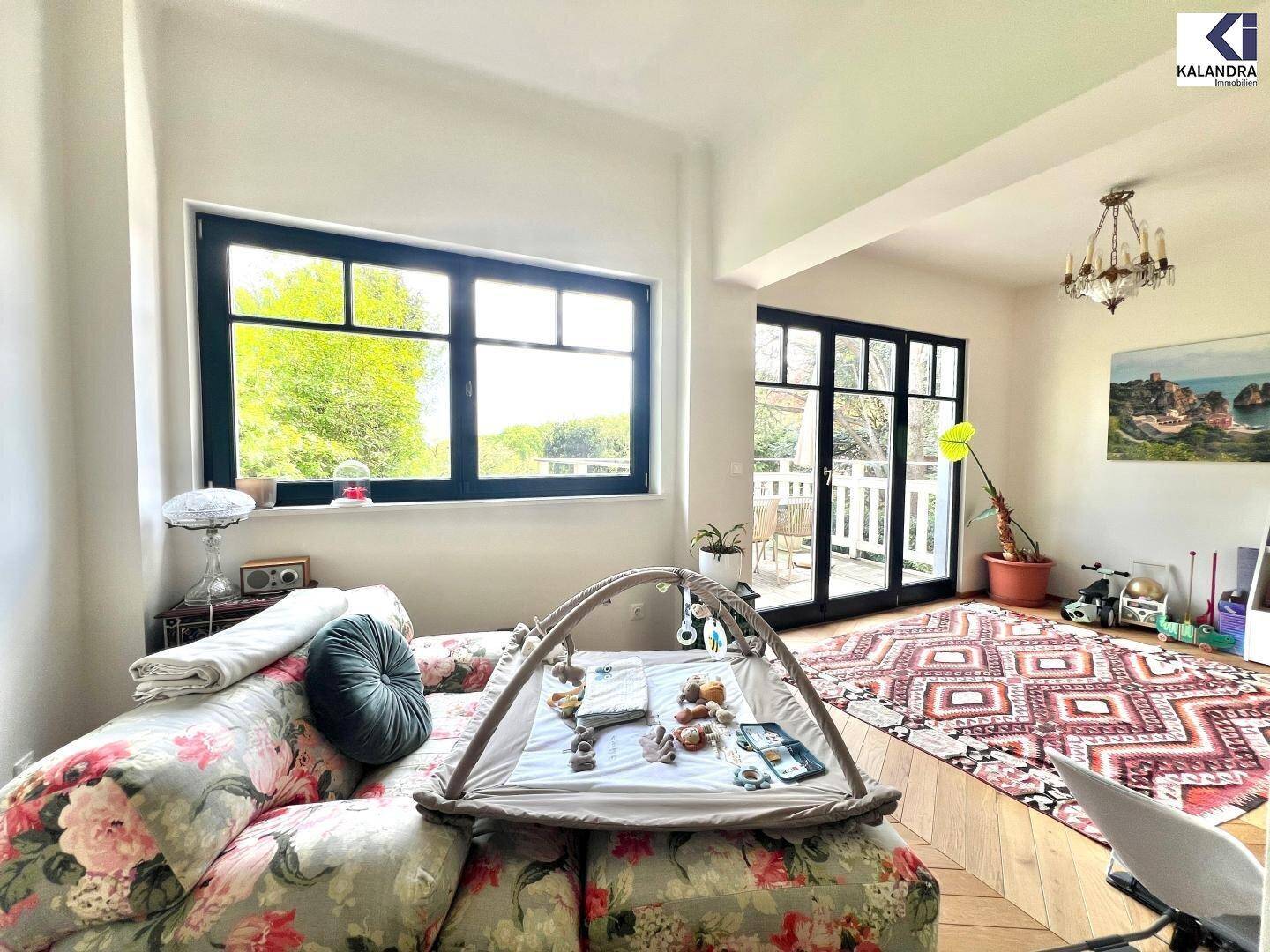 Gemütliches Wohnzimmer mit floralem Sofa, großen Fenstern und Zugang zu einem Außenbereich.