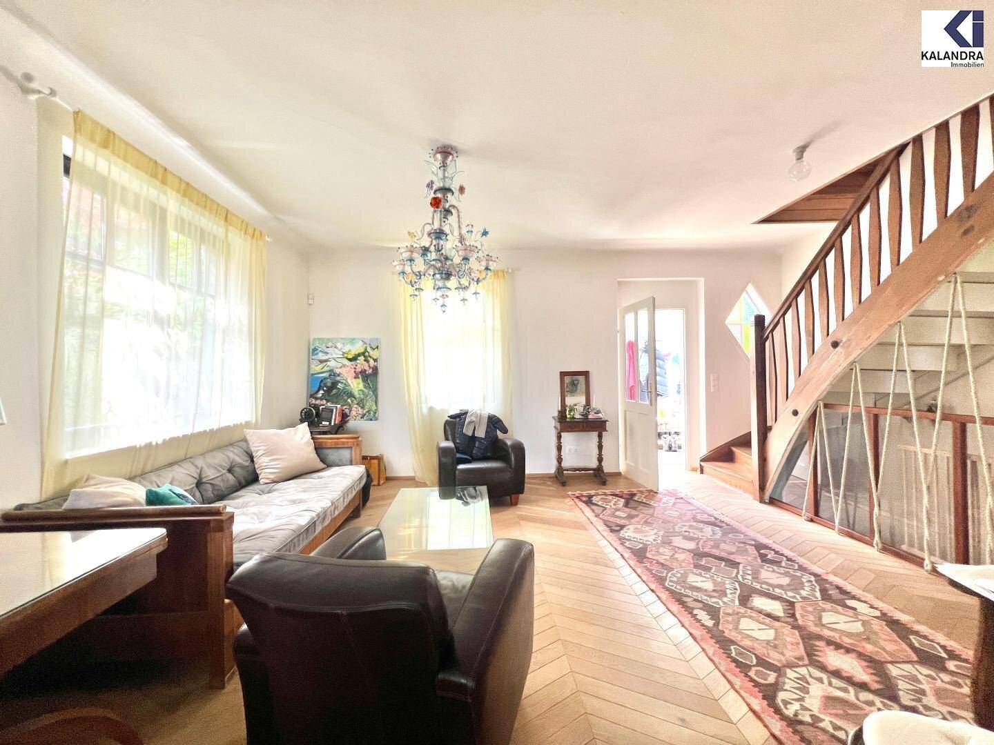 Gemütliches Wohnzimmer mit Sitzgelegenheiten, Holztreppe und einem auffälligen Kronleuchter.