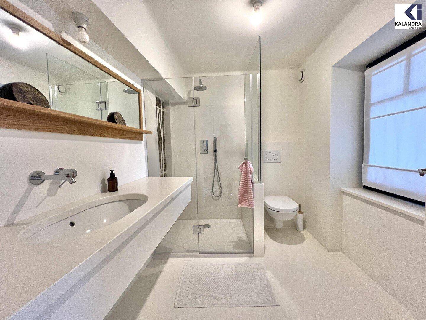 Helles Badezimmer mit moderner Dusche, Einzelwaschbecken, Toilette und Fenster für Tageslicht.