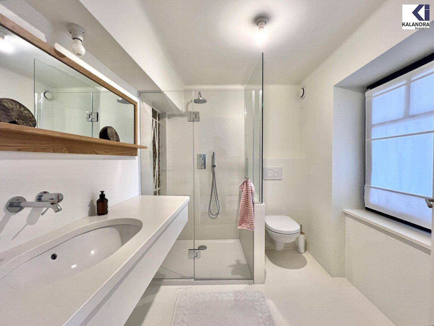Helles Badezimmer mit moderner Dusche, Einzelwaschbecken, Toilette und Fenster für Tageslicht.
