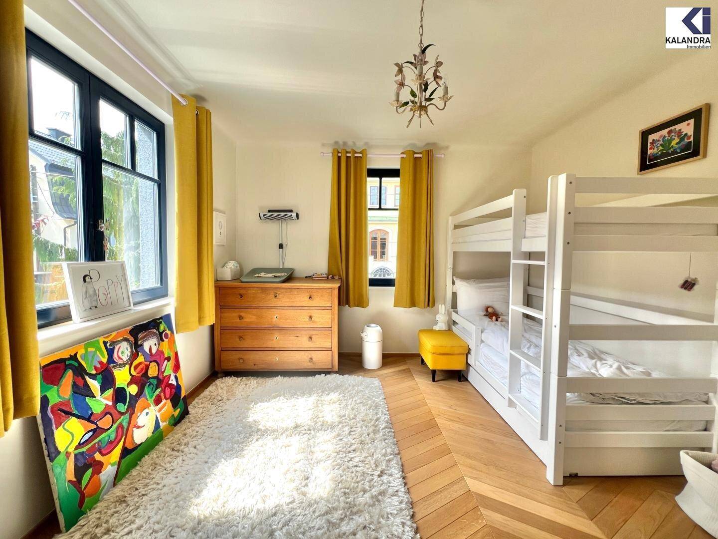 Kinderzimmer mit Etagenbett, Kommode und farbenfrohem Teppich auf Fischgrätparkett.