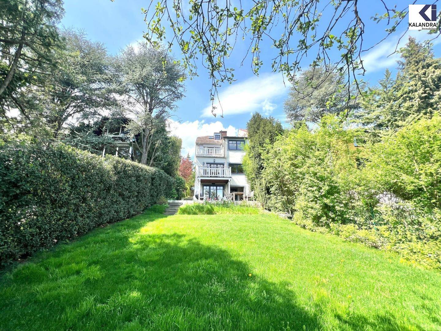 Weitläufiger Garten mit Rasenfläche und Blick auf die Rückseite des Hauses mit Balkonen.