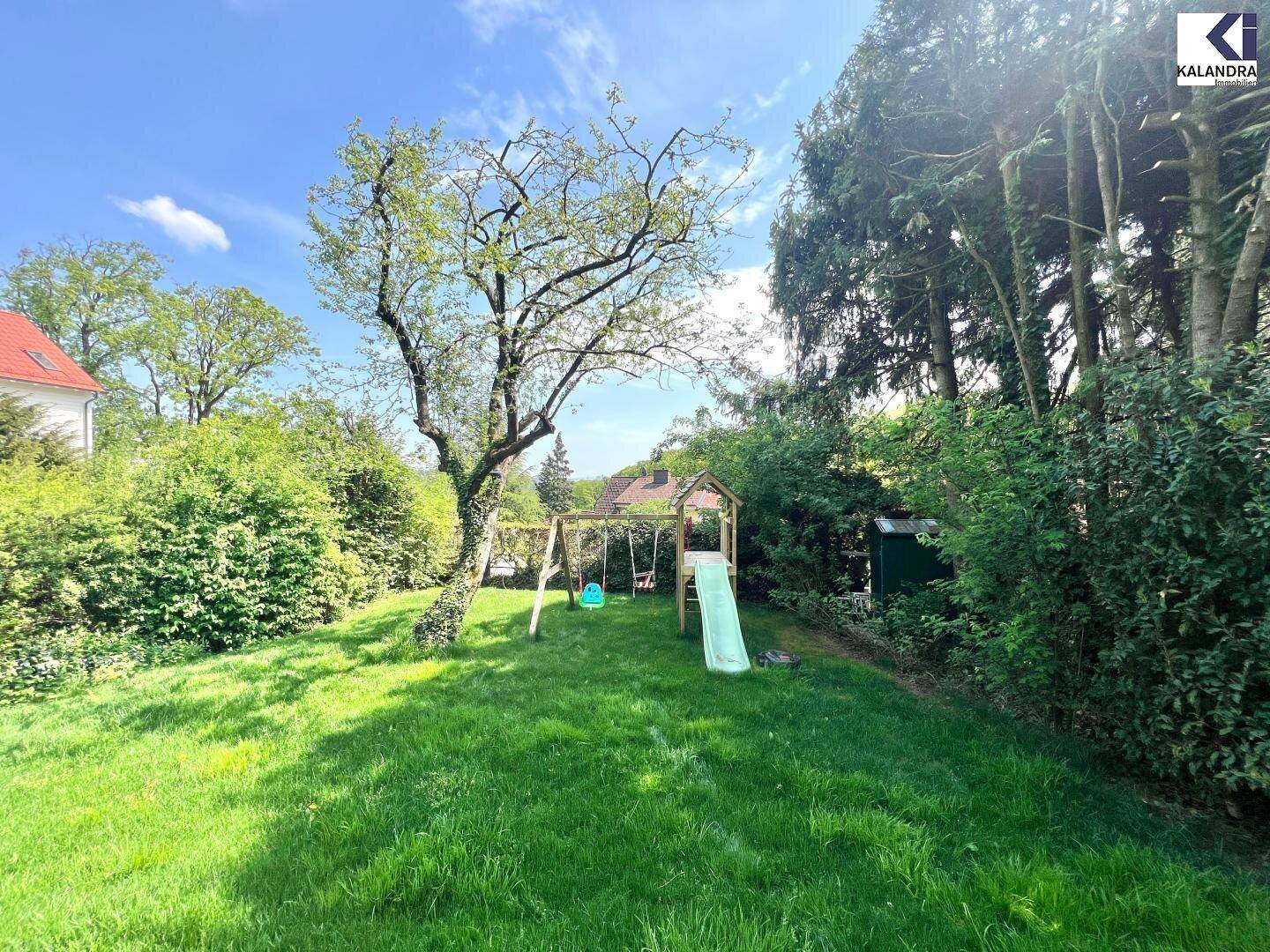 Seitlicher Gartenbereich mit Kinderspielplatz, altem Baum und einem kleinen Geräteschuppen.