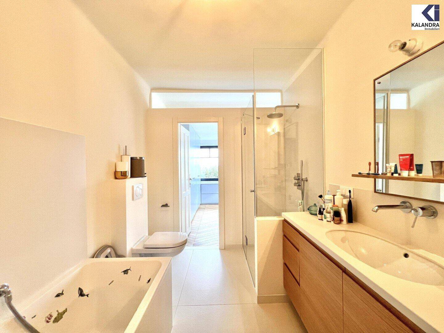 Geräumiges Badezimmer mit Badewanne, Dusche und Holzwaschtisch, blickt auf einen angrenzenden Raum.