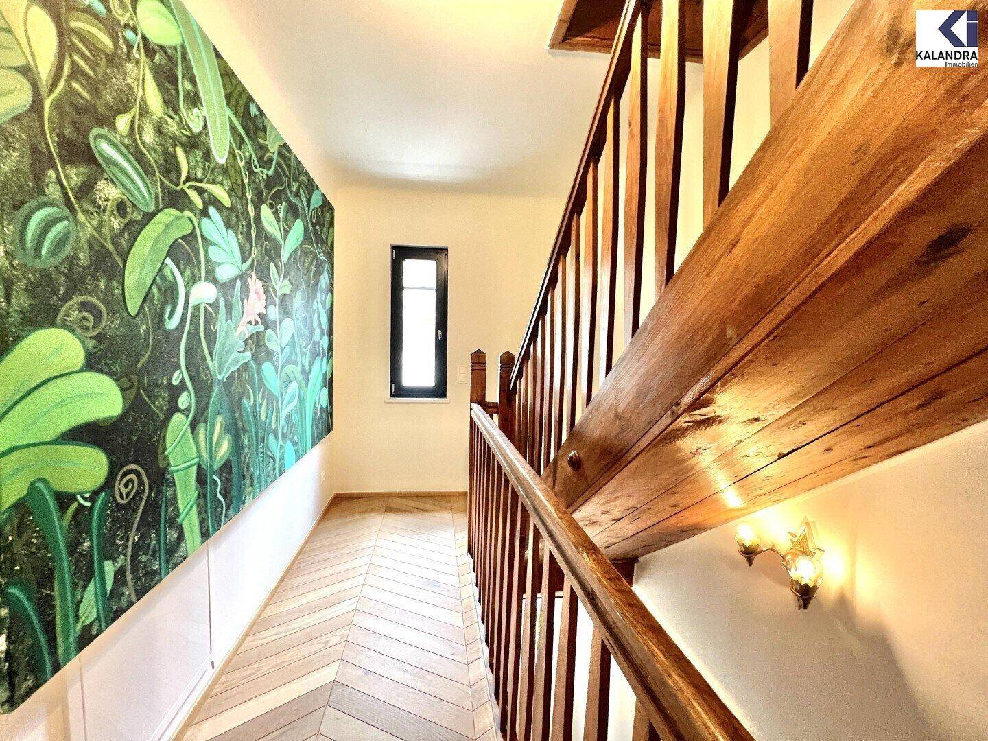 Heller Flur mit Holztreppe und einem großen, auffälligen Kunstwerk an der Wand.