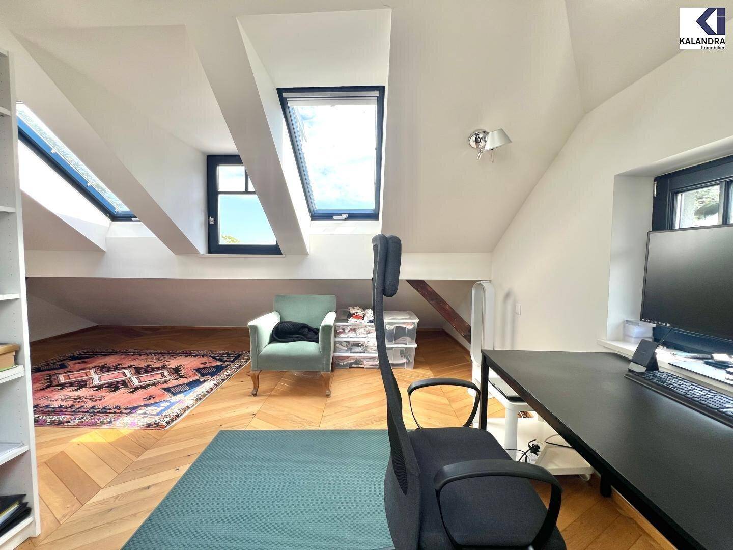 Helles Dachgeschoss-Büro mit schrägen Decken, Dachfenstern und Fischgrätparkettboden.