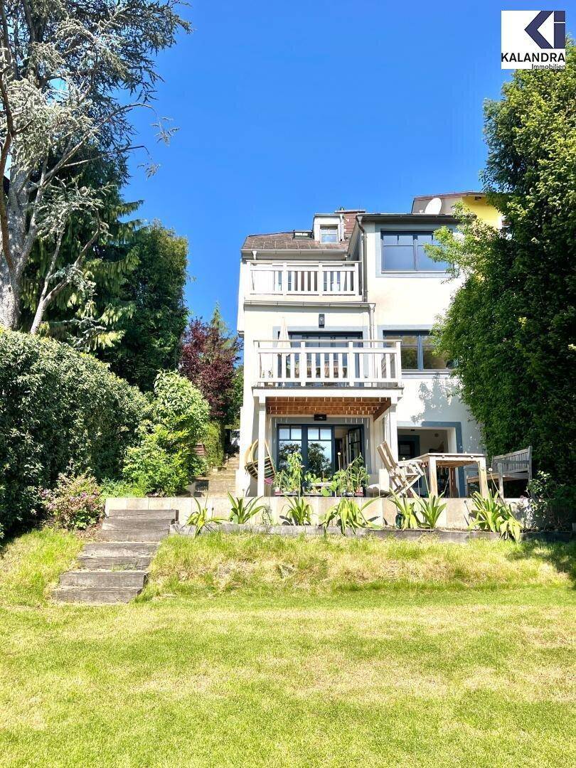 Rückansicht des Hauses mit mehreren Balkonen und einem gepflegten Garten mit Rasenfläche.