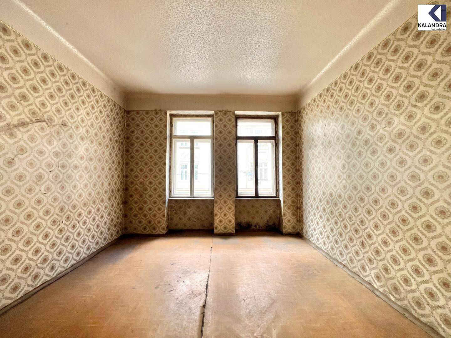 Sanierungsbedürftiger Raum mit alter Mustertapete und Holzboden, der auf eine Modernisierung wartet.