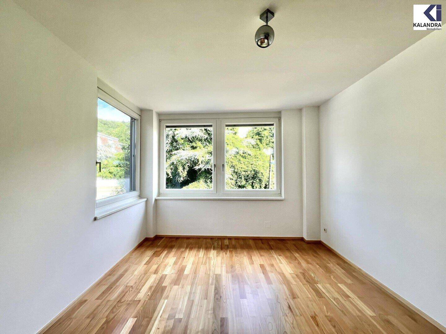 Helles Schlafzimmer mit Holzboden und großen Fenstern, die viel Tageslicht hereinlassen.