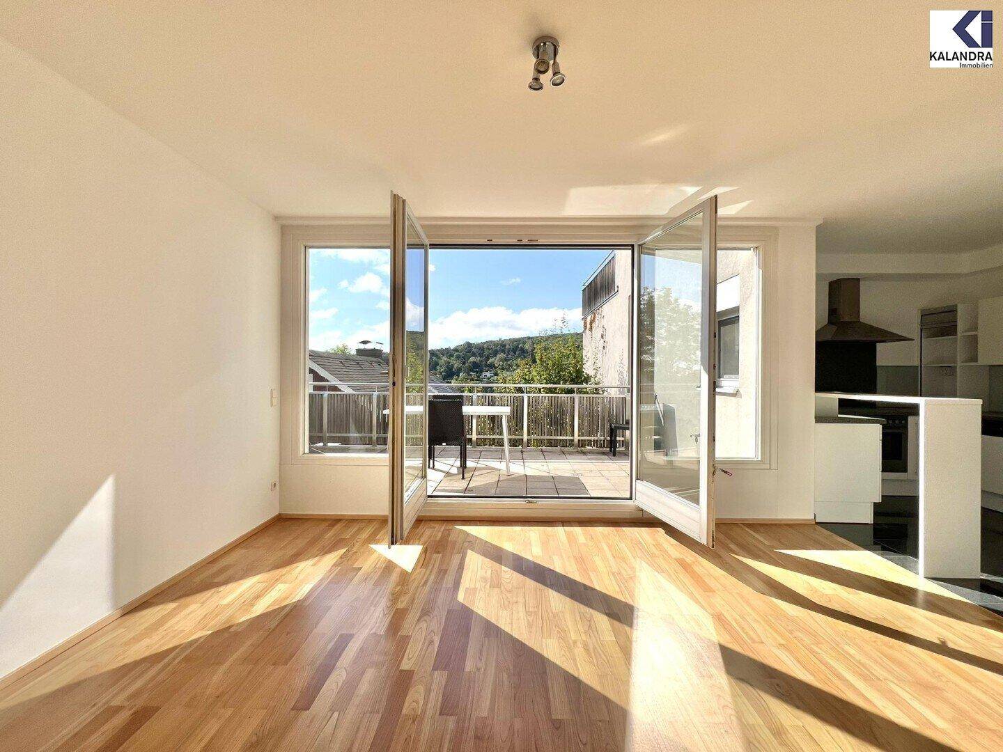 Lichtdurchflutetes Wohnzimmer mit Holzboden und großen Fenstern, die auf einen Balkon führen.