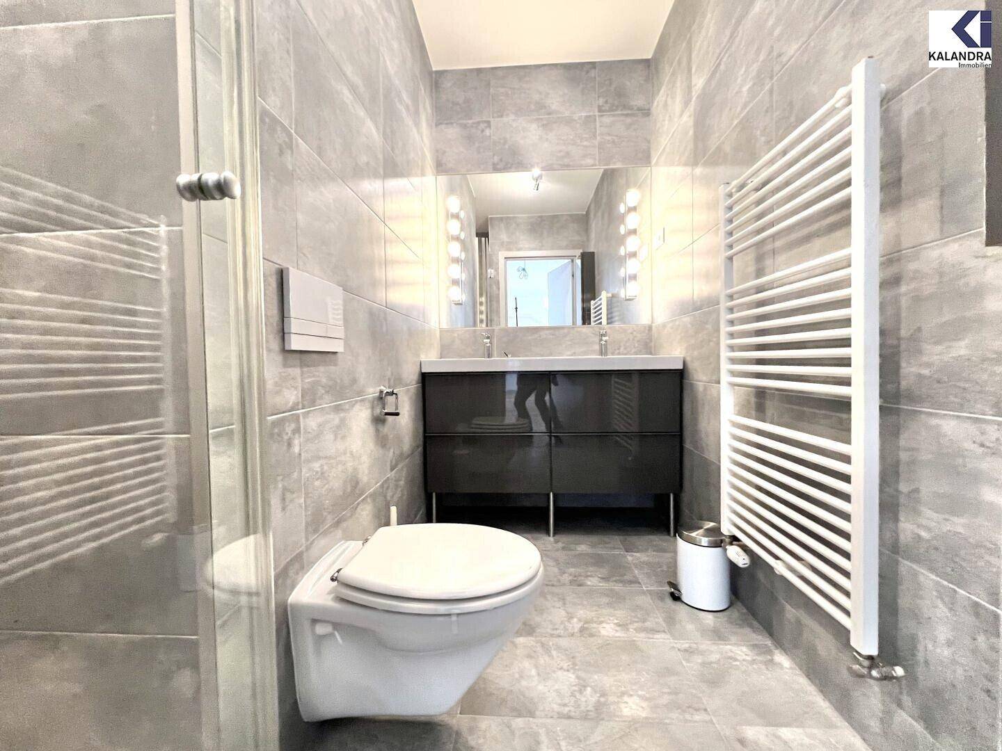 Modernes Badezimmer mit grauen Fliesen, Doppelwaschbecken, Wand-WC und beheiztem Handtuchhalter.