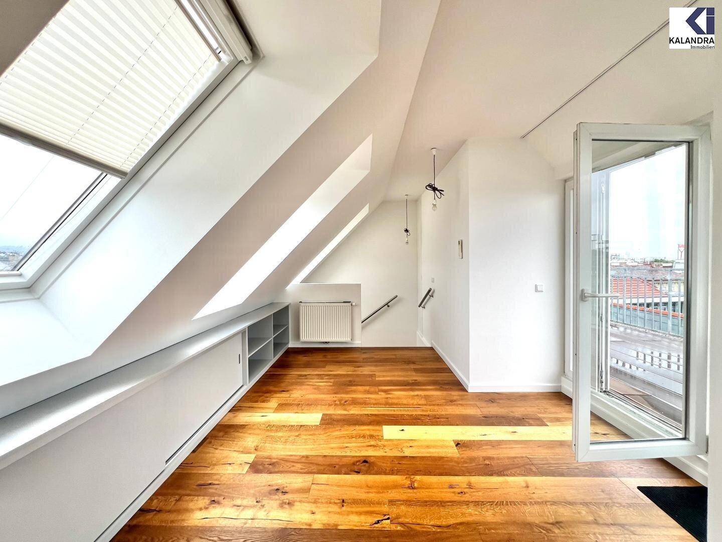 Heller Dachgeschossraum mit Holzboden, mehreren Dachfenstern und Zugang zu einem Außenbereich.